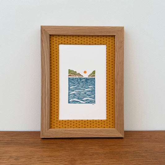 Framed artwork with a landscape design on a wooden surface and white wall background