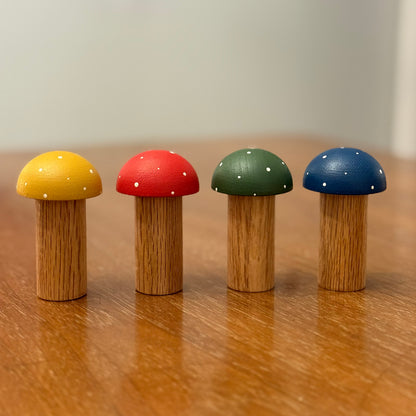 Four colorful wooden mushroom playing pegs on a wooden surface. The playing pegs are yellow, red, green and blue.