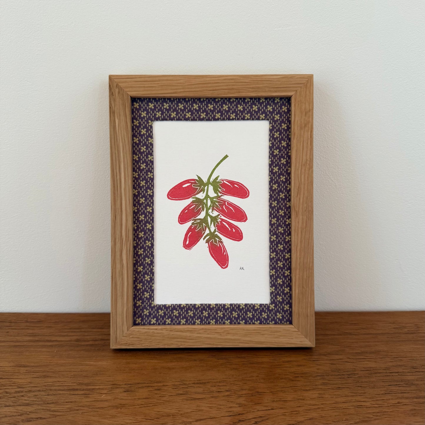 Framed artwork with a tomato design on a wooden surface and white wall background