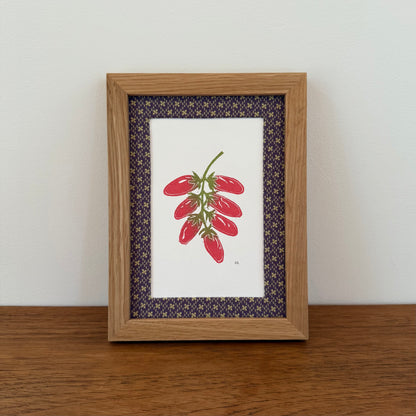 Framed artwork with a tomato design on a wooden surface and white wall background