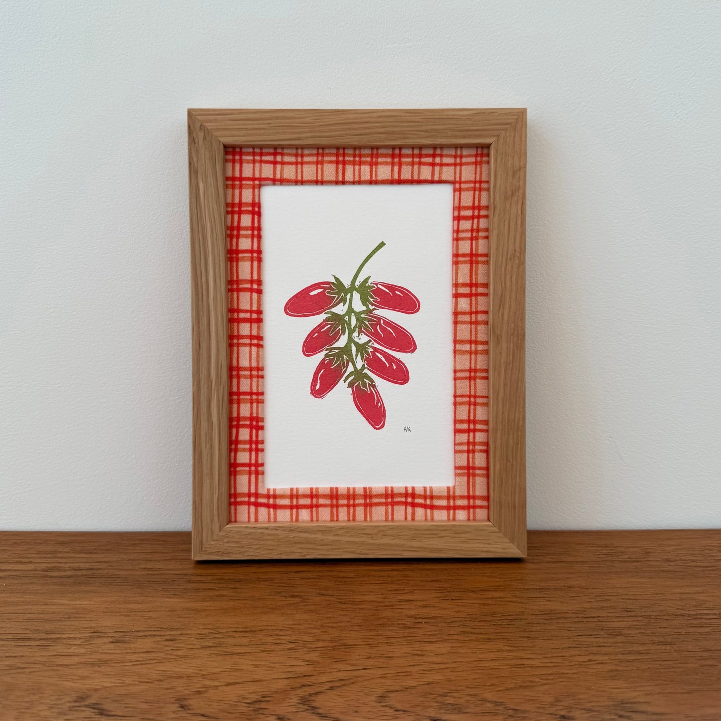 Framed artwork with a tomato design on a wooden surface and white wall background