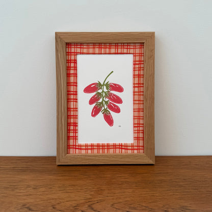 Framed artwork with a tomato design on a wooden surface and white wall background