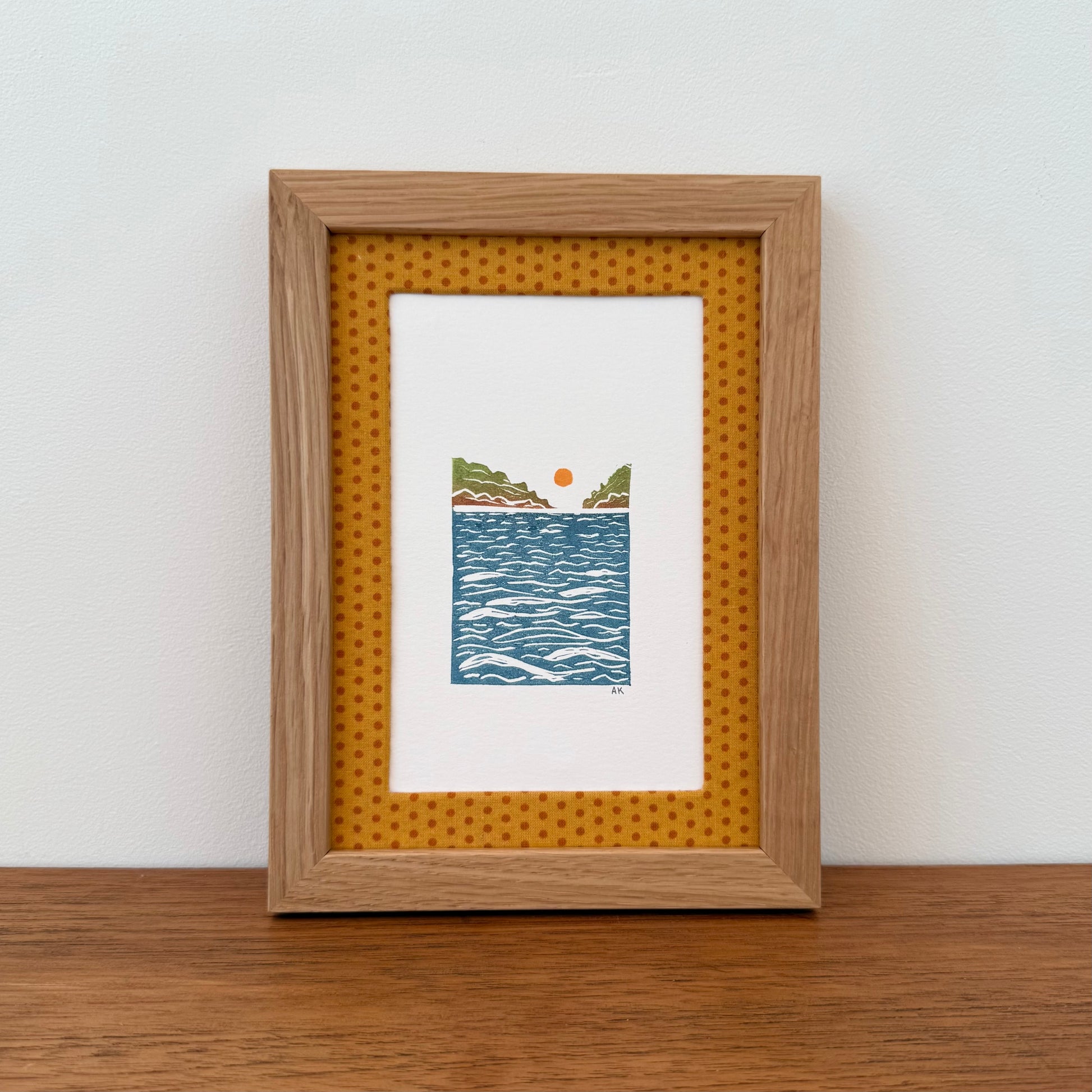 Framed artwork with a landscape design on a wooden surface and white wall background