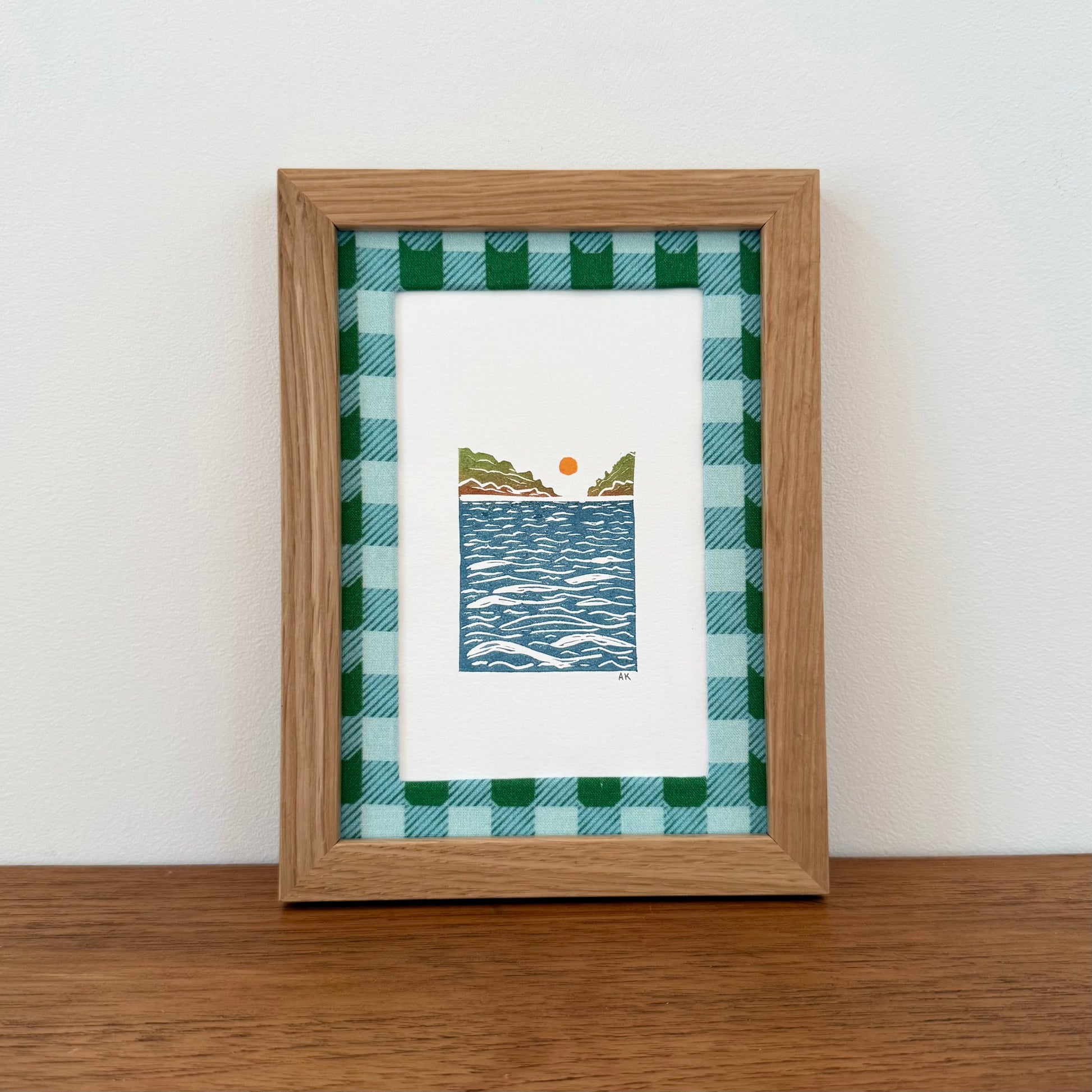 Framed artwork with a landscape design on a wooden surface and white wall background