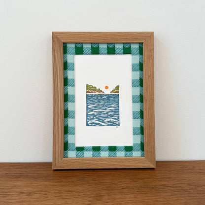 Framed artwork with a landscape design on a wooden surface and white wall background