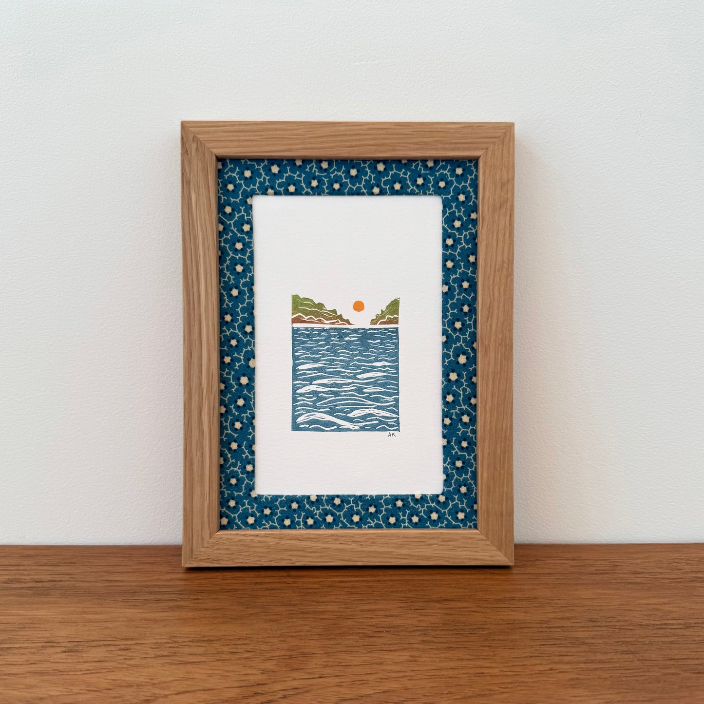 Framed artwork with a landscape design on a wooden surface and white wall background