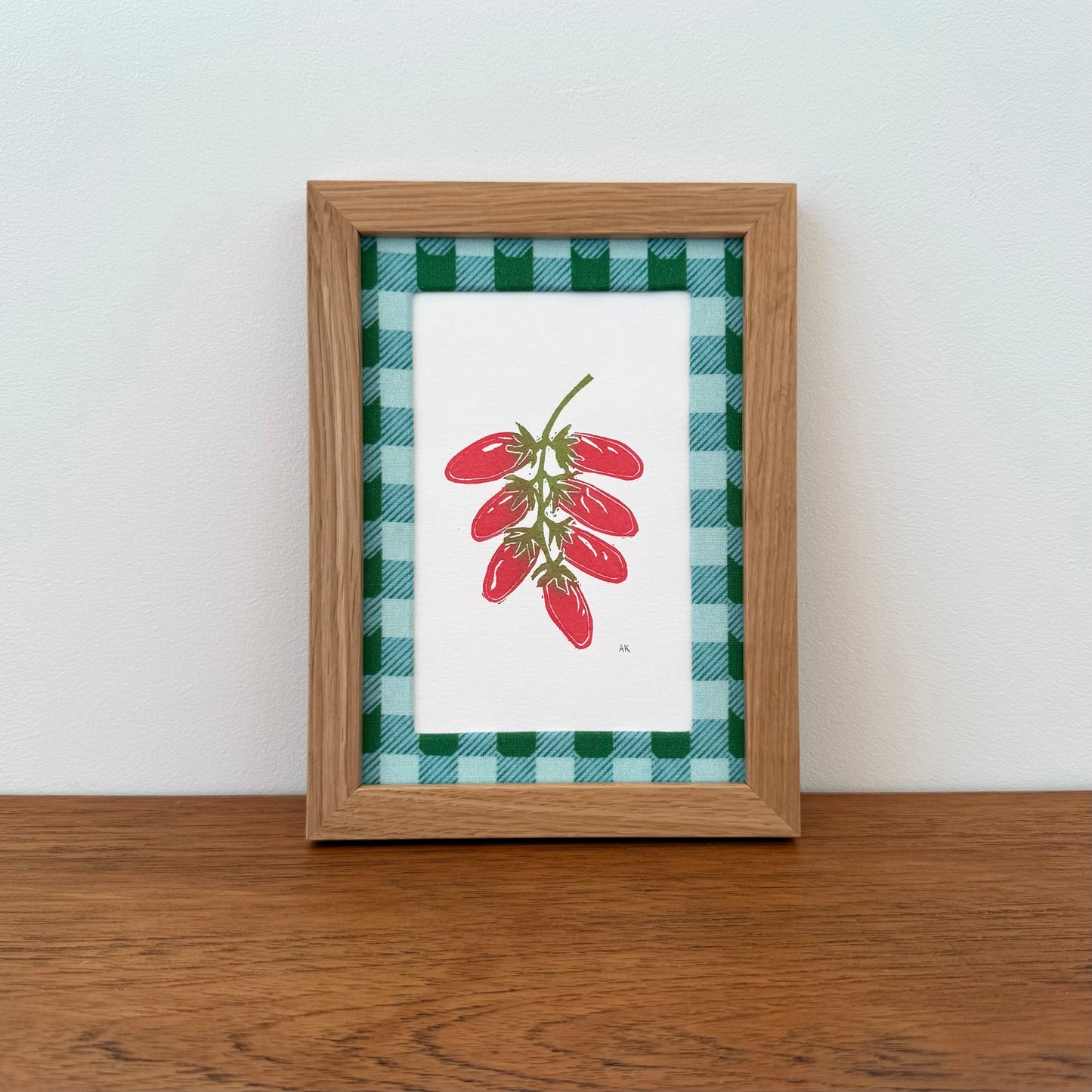 Framed artwork with a tomato design on a wooden surface and white wall background