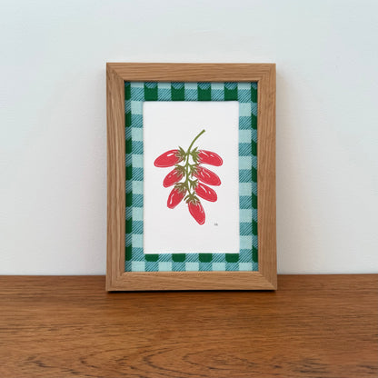 Framed artwork with a tomato design on a wooden surface and white wall background