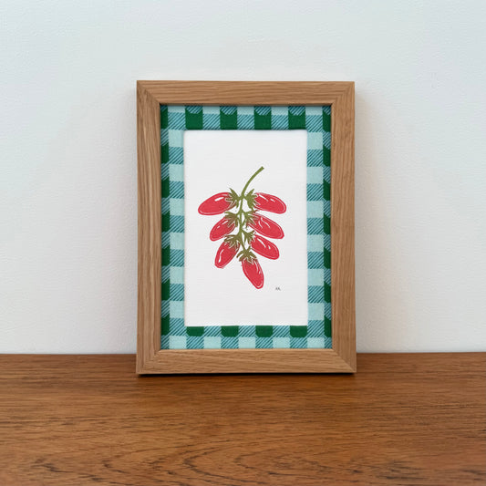 Framed artwork with a tomato design on a wooden surface and white wall background