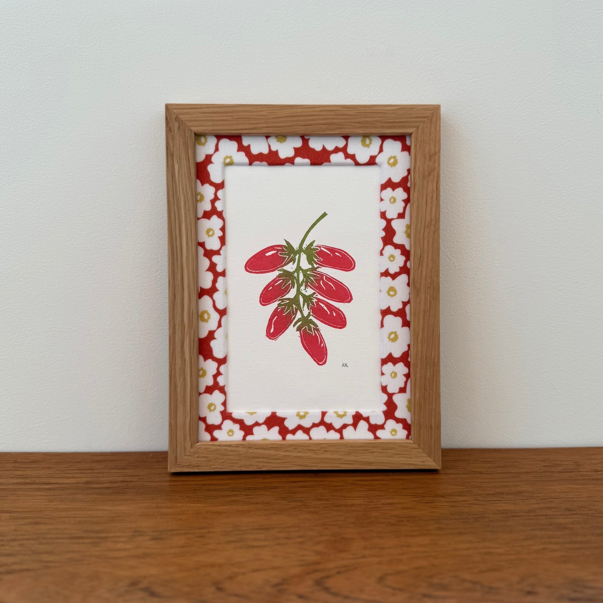 Framed artwork with a tomato design on a wooden surface and white wall background