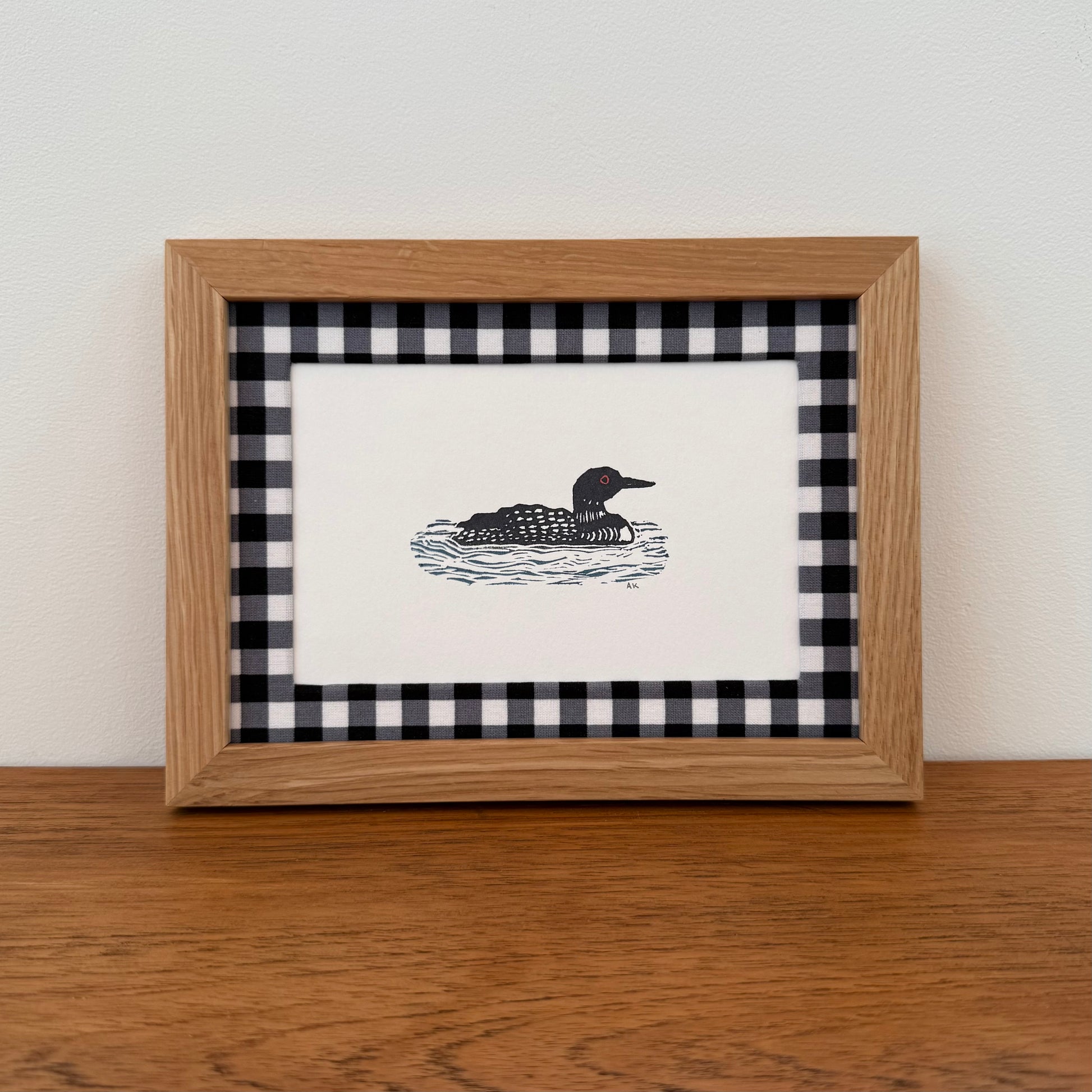 Framed artwork with a loon design on a wooden surface and white wall background