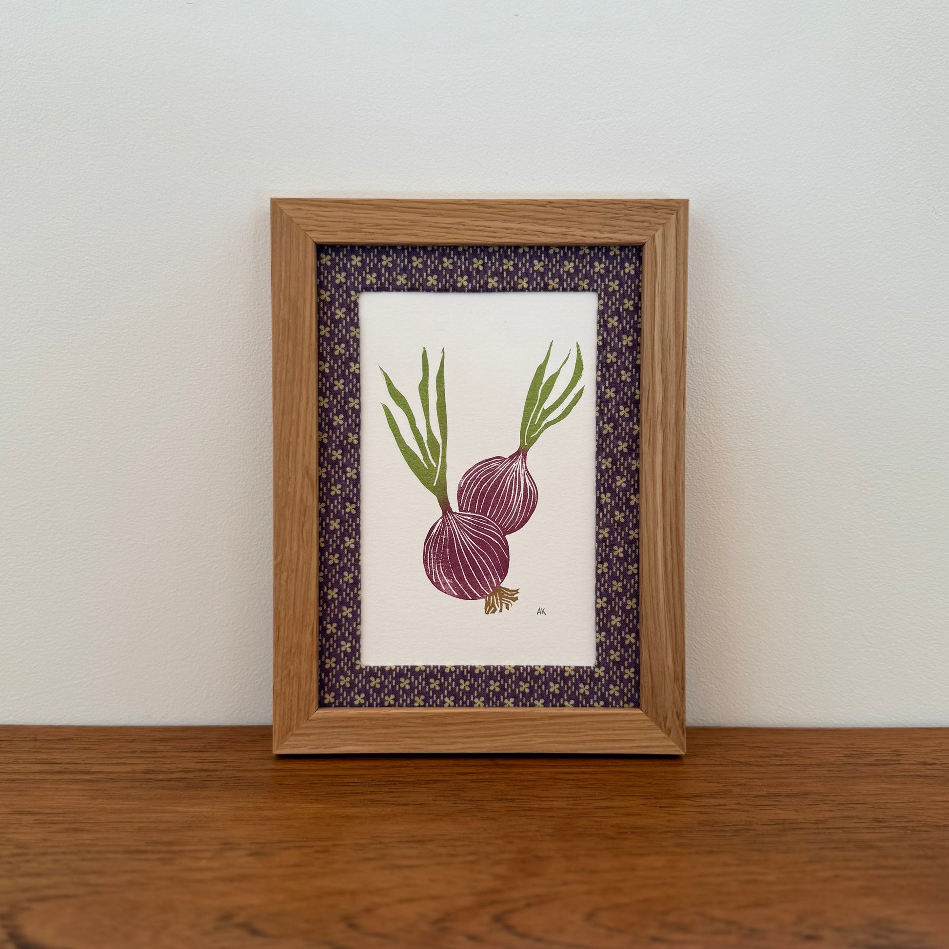 Framed artwork with a red onion design on a wooden surface and white wall background