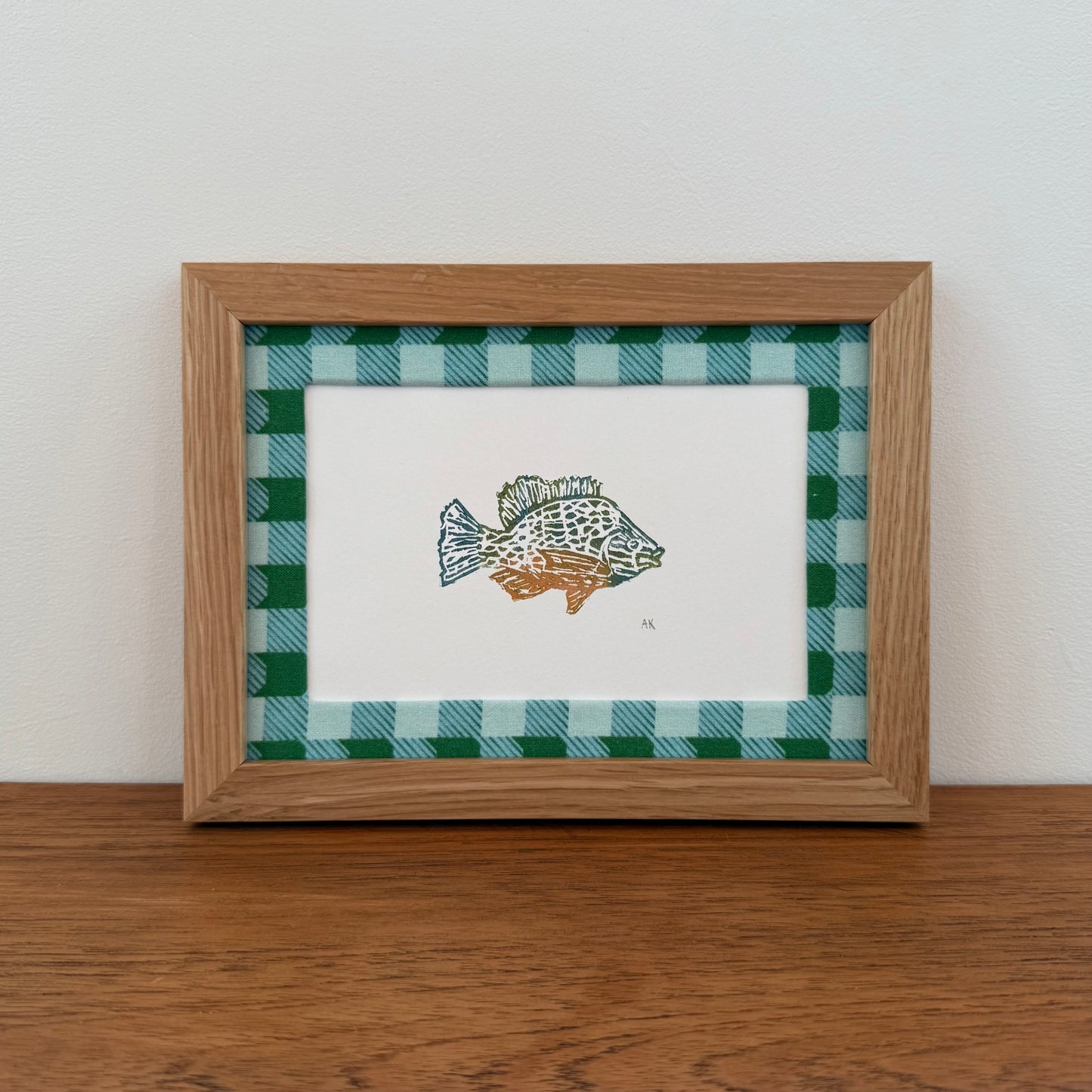 Framed artwork with a sunfish design on a wooden surface and white wall background