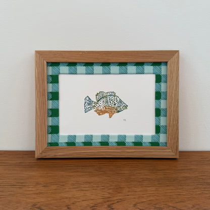 Framed artwork with a sunfish design on a wooden surface and white wall background