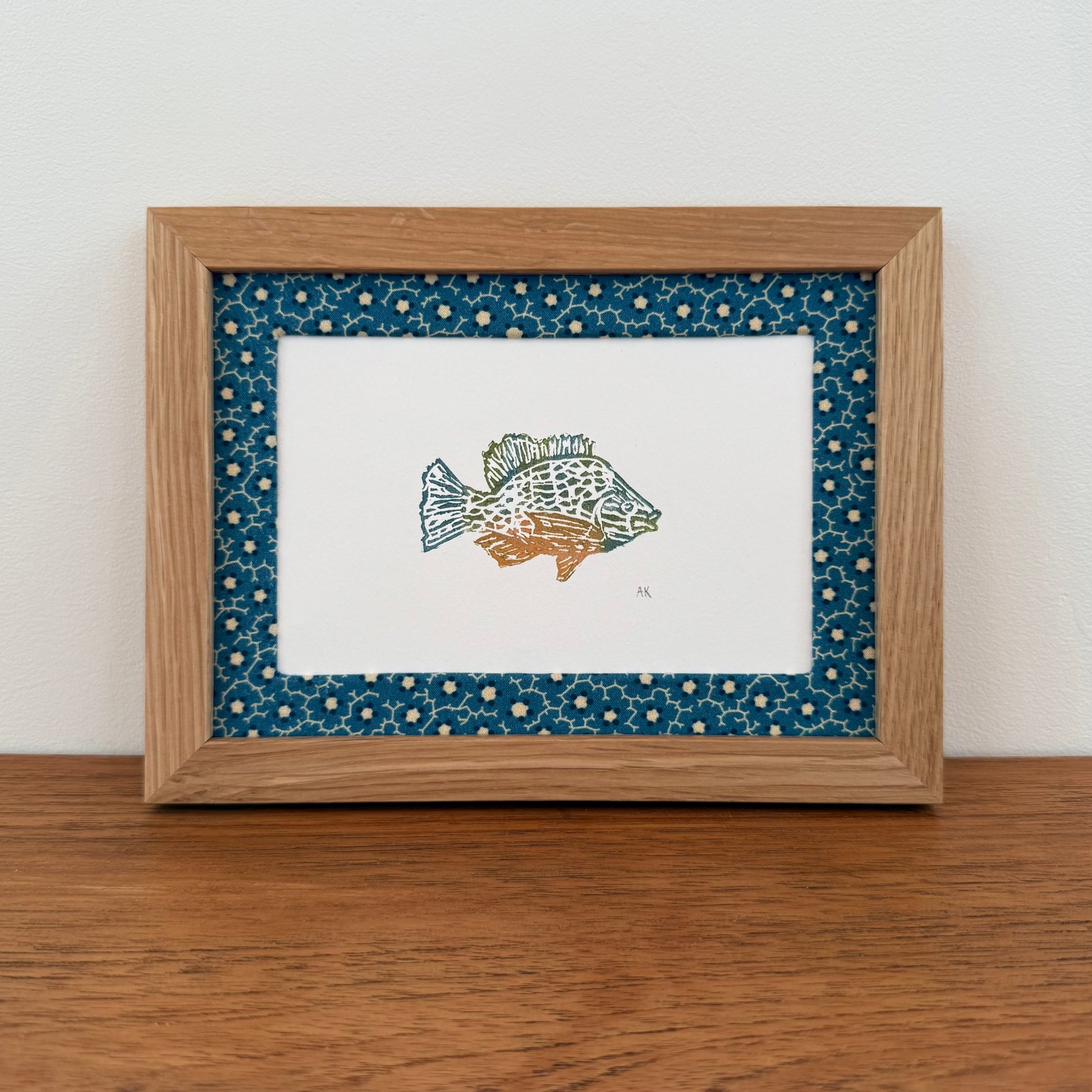 Framed artwork with a sunfish design on a wooden surface and white wall background