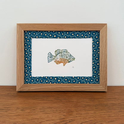 Framed artwork with a sunfish design on a wooden surface and white wall background