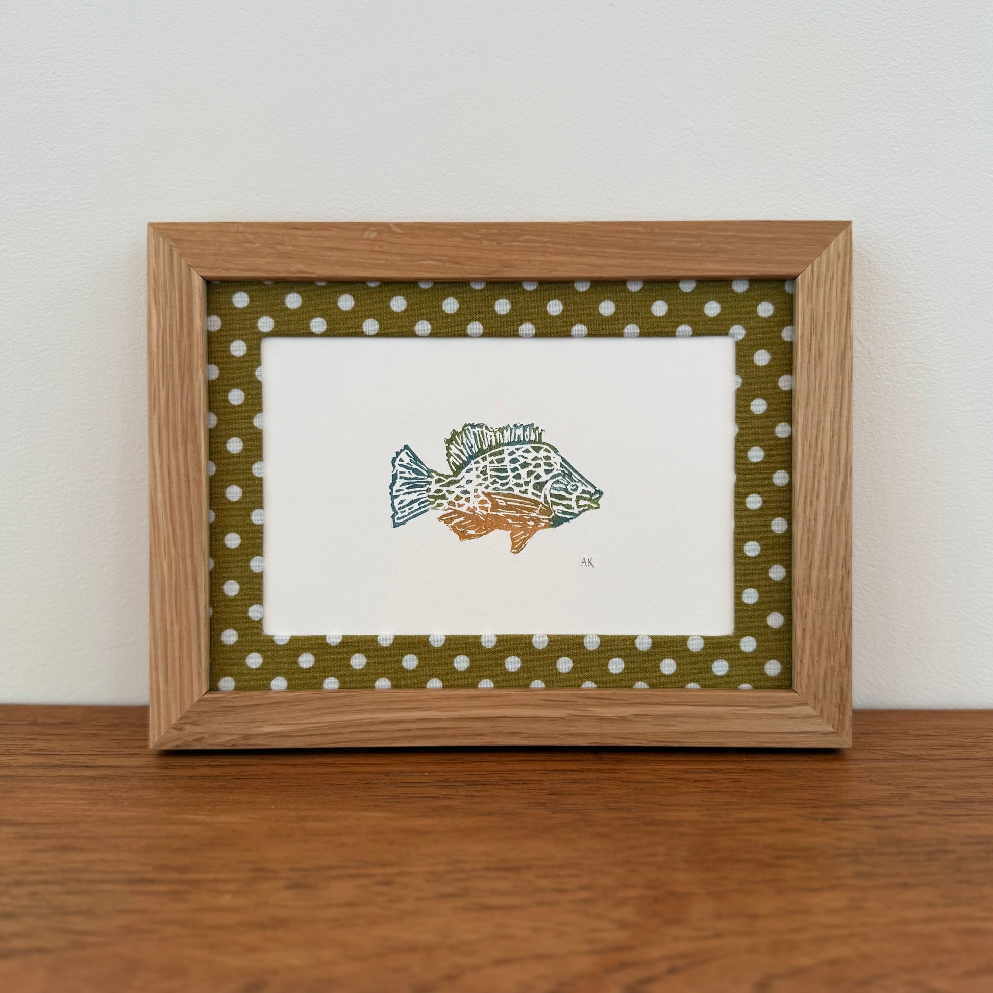 Framed artwork with a sunfish design on a wooden surface and white wall background