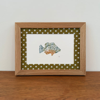 Framed artwork with a sunfish design on a wooden surface and white wall background
