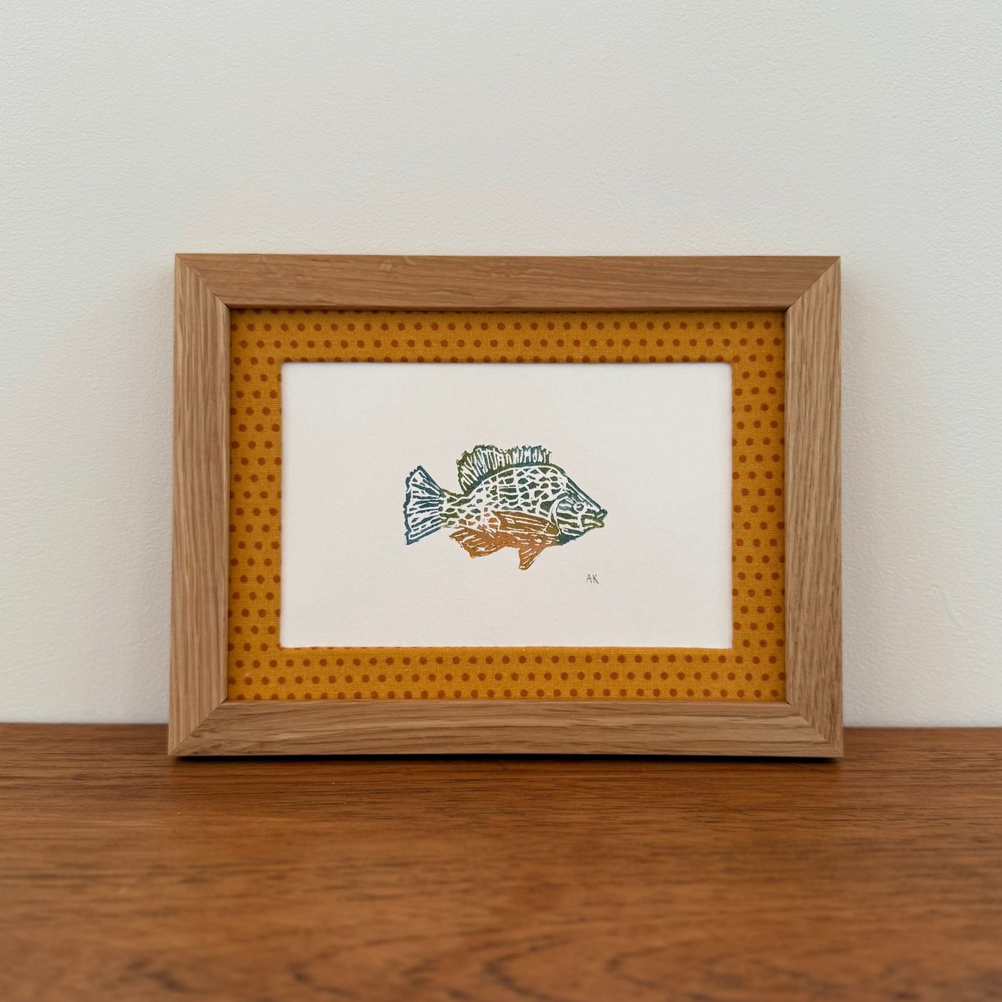 Framed artwork with a sunfish design on a wooden surface and white wall background
