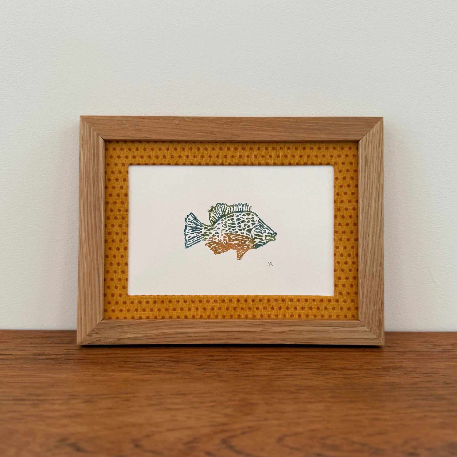 Framed artwork with a sunfish design on a wooden surface and white wall background