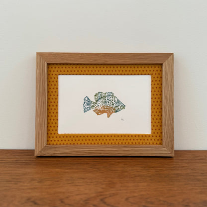 Framed artwork with a sunfish design on a wooden surface and white wall background