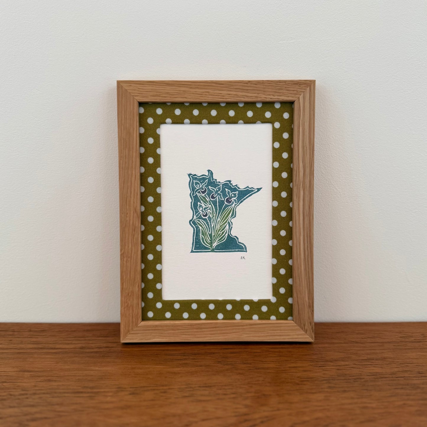Framed artwork with a Minnesota state design on a wooden surface and white wall background