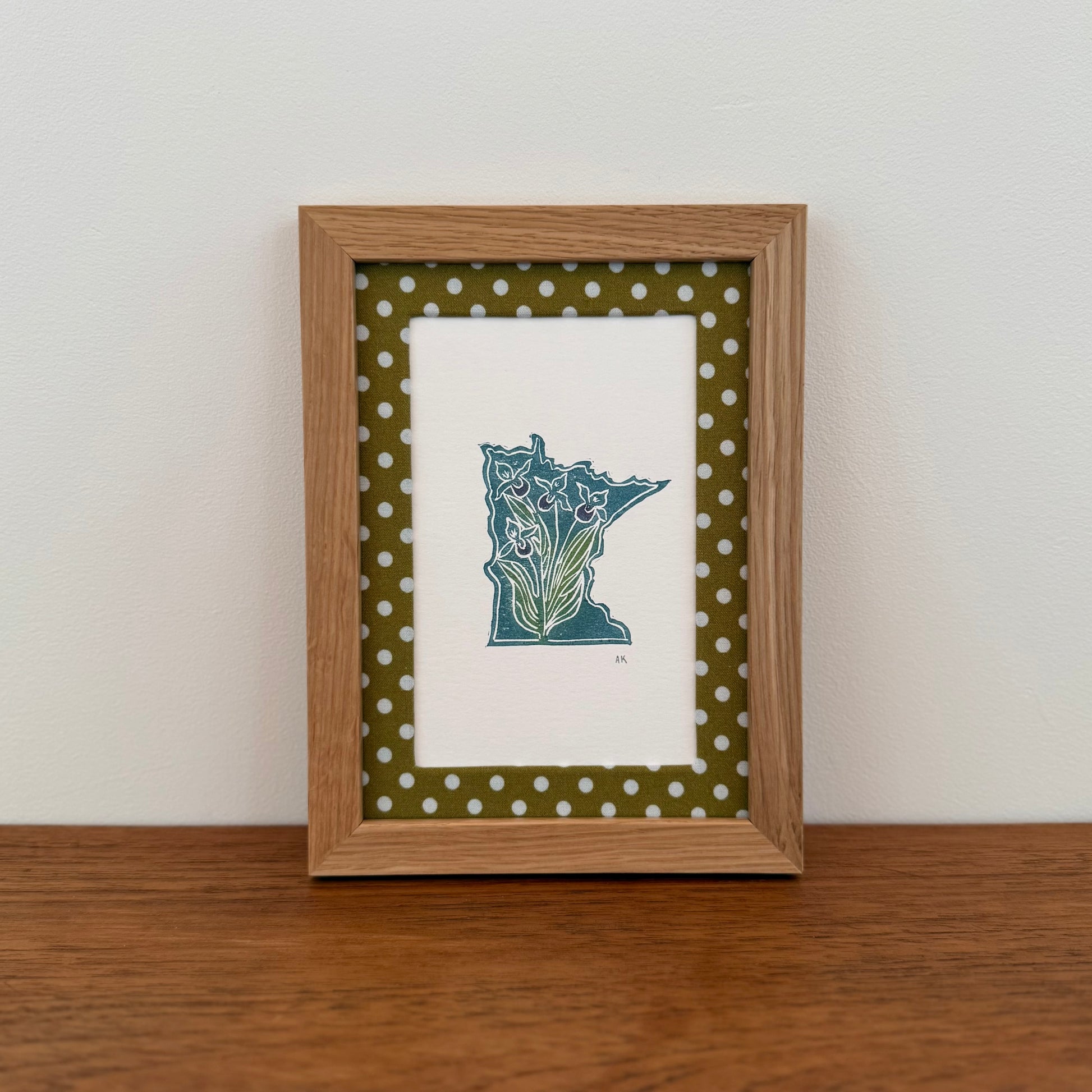 Framed artwork with a Minnesota state design on a wooden surface and white wall background