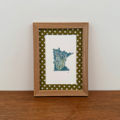 Framed artwork with a Minnesota state design on a wooden surface and white wall background
