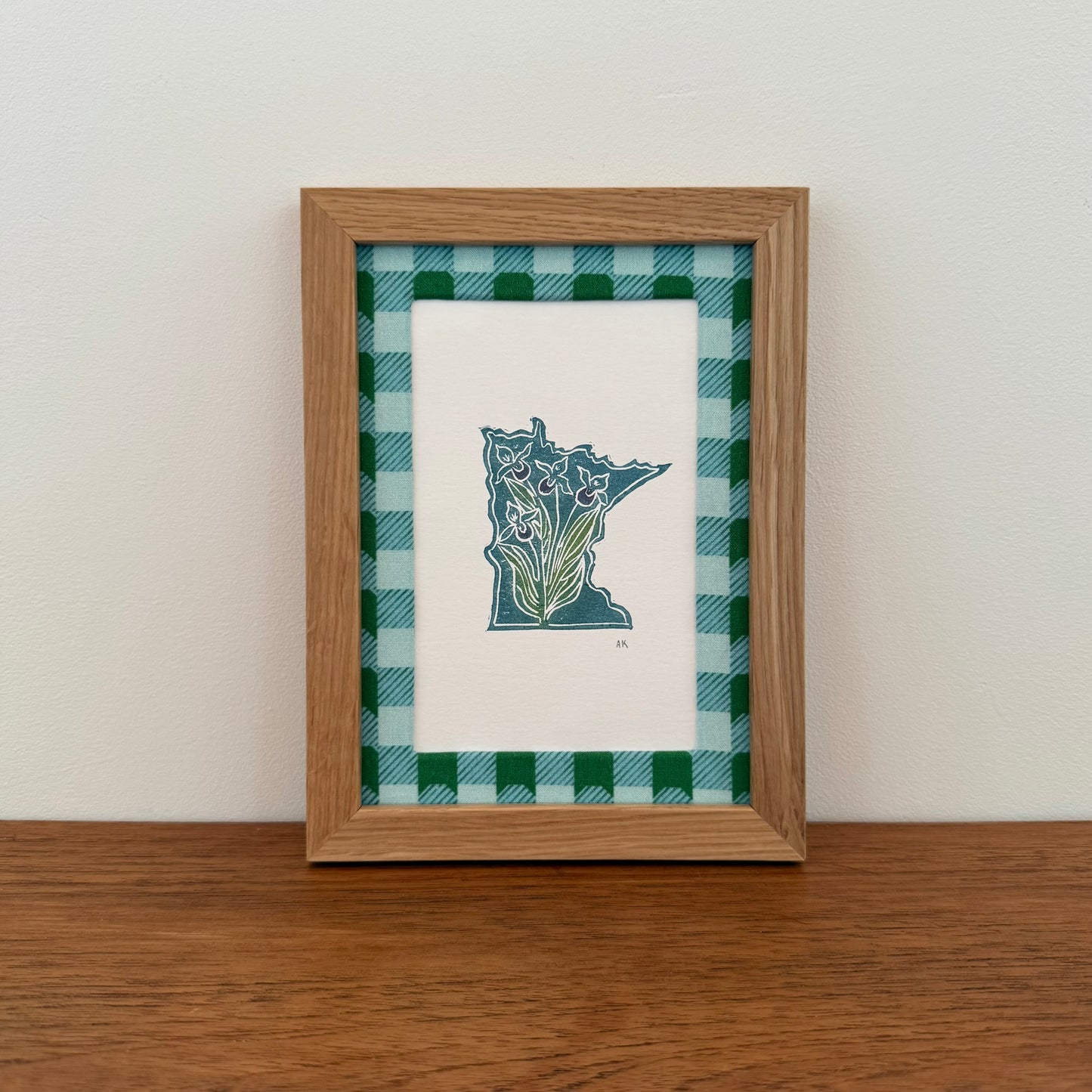 Framed artwork with a Minnesota state design on a wooden surface and white wall background
