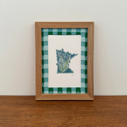Framed artwork with a Minnesota state design on a wooden surface and white wall background