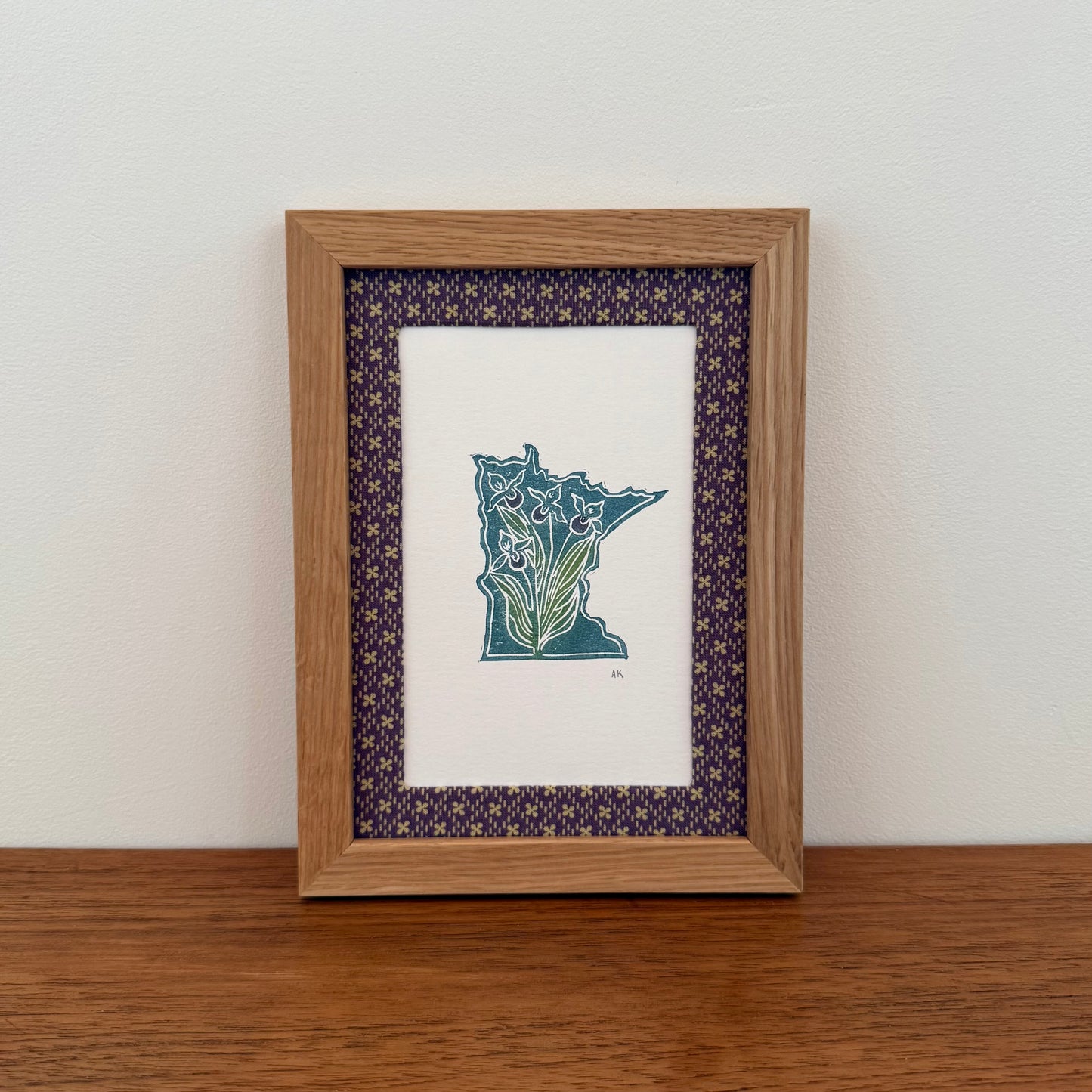 Framed artwork with a Minnesota state design on a wooden surface and white wall background