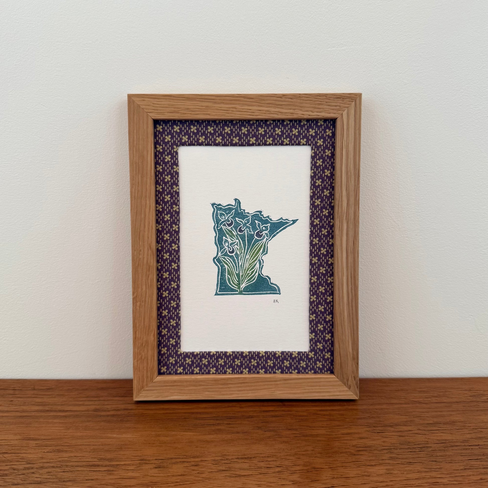 Framed artwork with a Minnesota state design on a wooden surface and white wall background