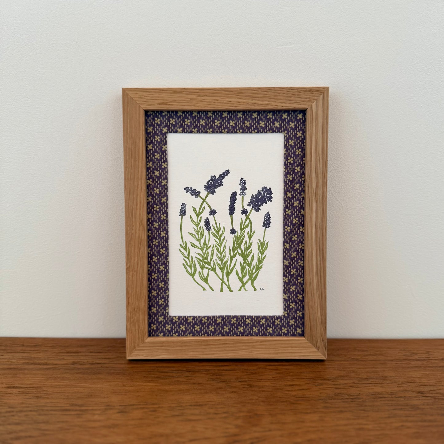 Framed artwork with a lavender design on a wooden surface and white wall background