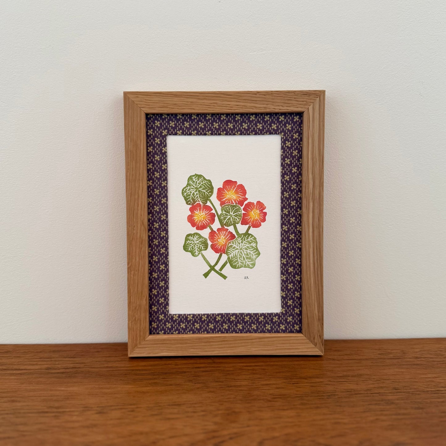 Framed artwork with a nasturtium design on a wooden surface and white wall background