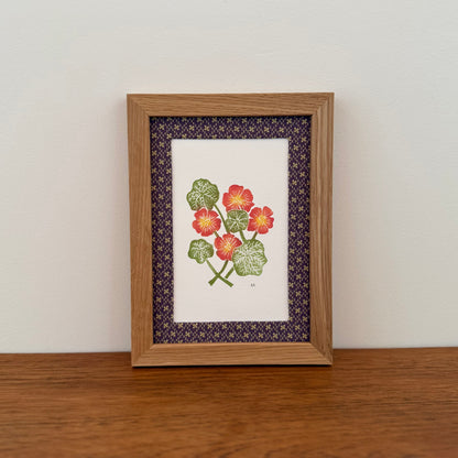 Framed artwork with a nasturtium design on a wooden surface and white wall background