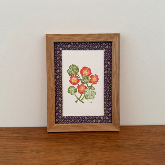 Framed artwork with a nasturtium design on a wooden surface and white wall background