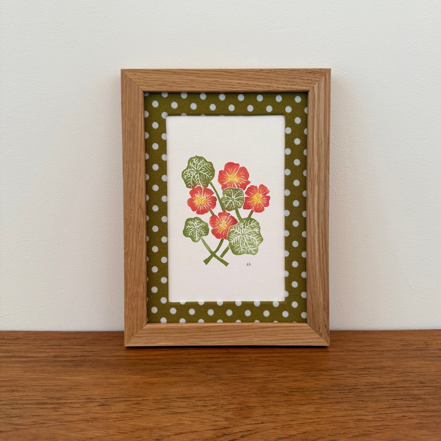 Framed artwork with a nasturtium design on a wooden surface and white wall background