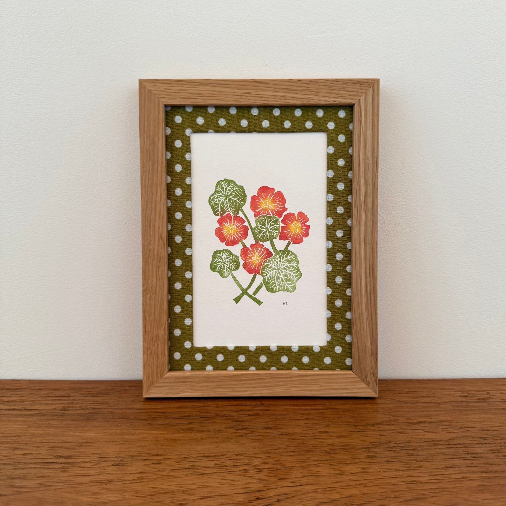 Framed artwork with a nasturtium design on a wooden surface and white wall background