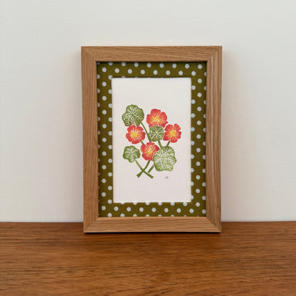 Framed artwork with a nasturtium design on a wooden surface and white wall background