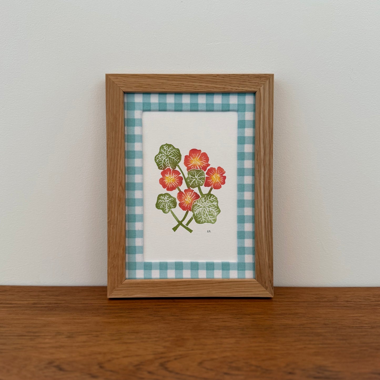 Framed artwork with a nasturtium design on a wooden surface and white wall background
