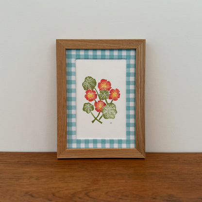 Framed artwork with a nasturtium design on a wooden surface and white wall background