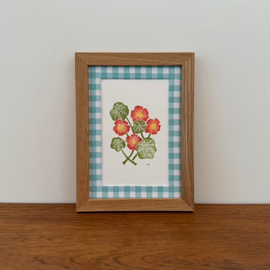 Framed artwork with a nasturtium design on a wooden surface and white wall background