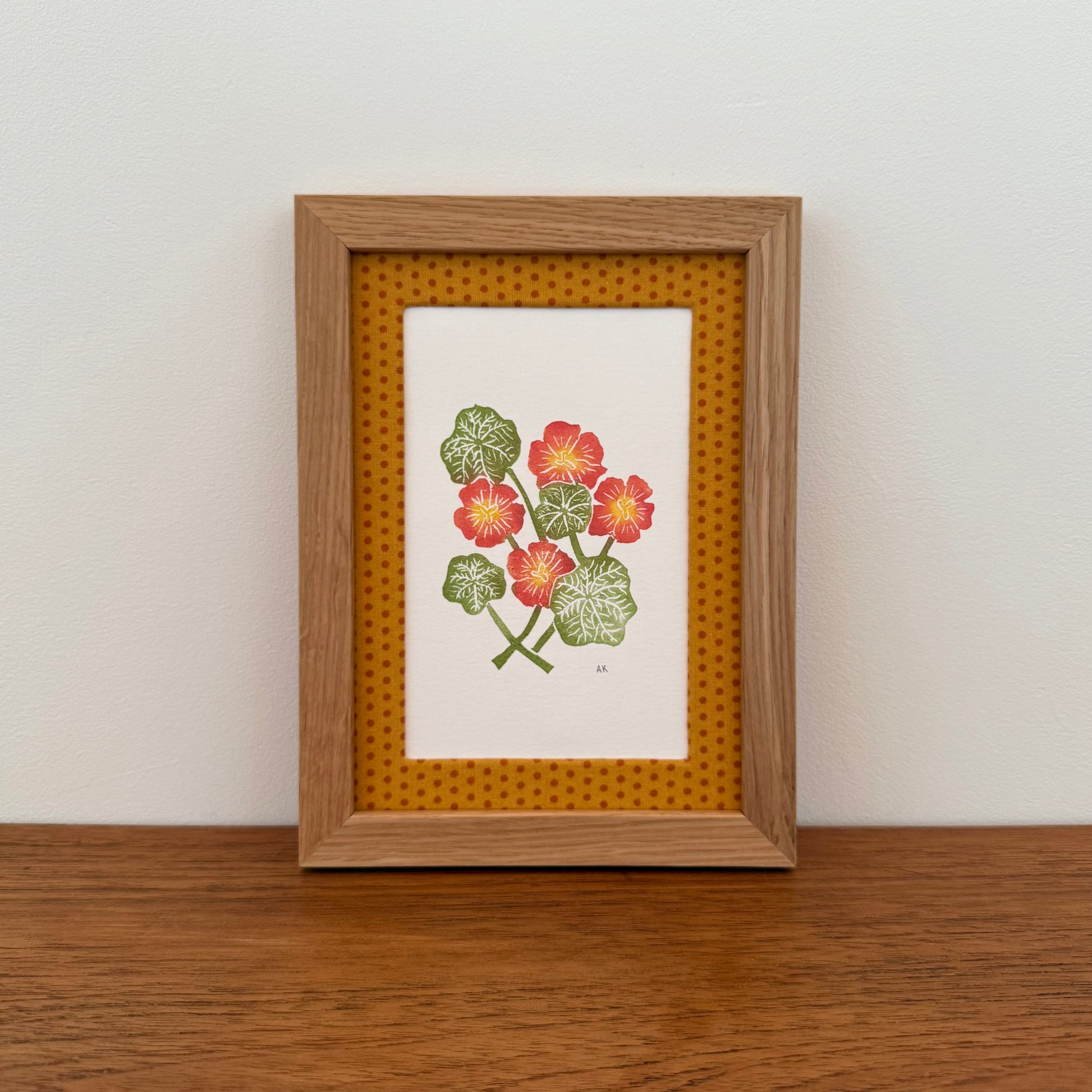 Framed artwork with a nasturtium design on a wooden surface and white wall background