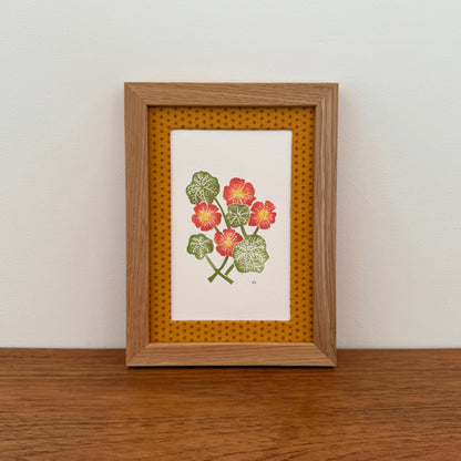 Framed artwork with a nasturtium design on a wooden surface and white wall background
