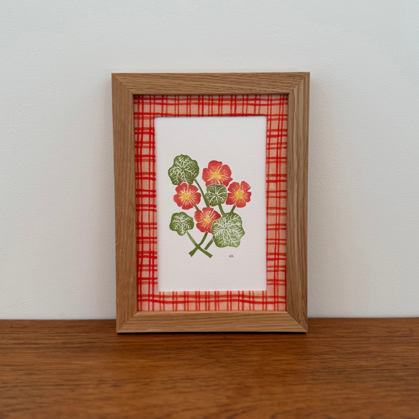 Framed artwork with a nasturtium design on a wooden surface and white wall background