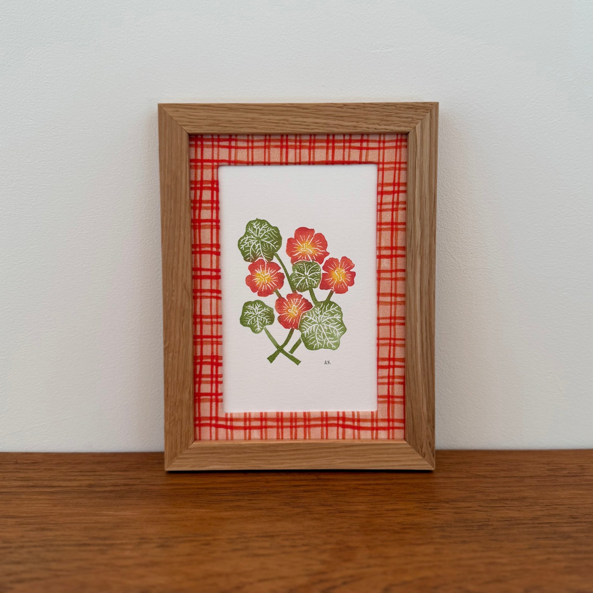 Framed artwork with a nasturtium design on a wooden surface and white wall background