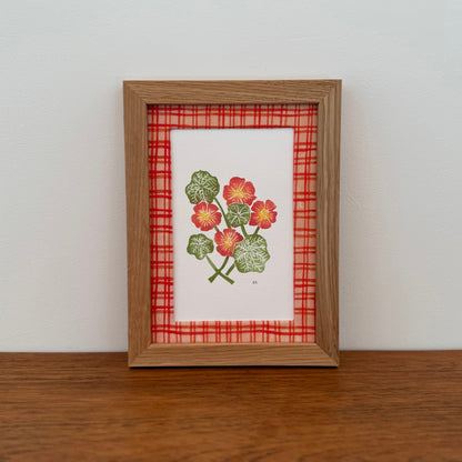 Framed artwork with a nasturtium design on a wooden surface and white wall background