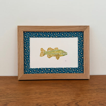 Framed artwork with a bass design on a wooden surface and white wall background
