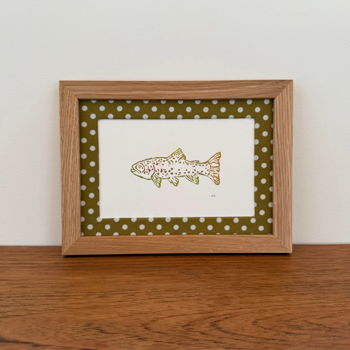 Framed artwork with a trout design on a wooden surface and white wall background