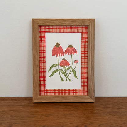 Framed artwork with an echinacea design on a wooden surface and white wall background